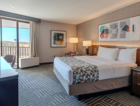 Bedroom at Valley Forge Casino Resort with a king bed and geometric throw, abstract art above the headboard, and a balcony overlooking wooded hills.