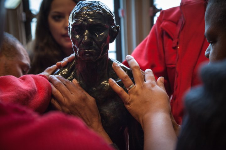 Visitors who have low visibility or blindness touch a sculpture at the Rodin Museum.