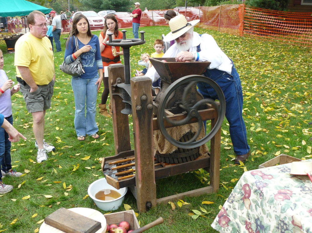 Man pressing apples for cider with guests watching at the Apple Butter Frolic