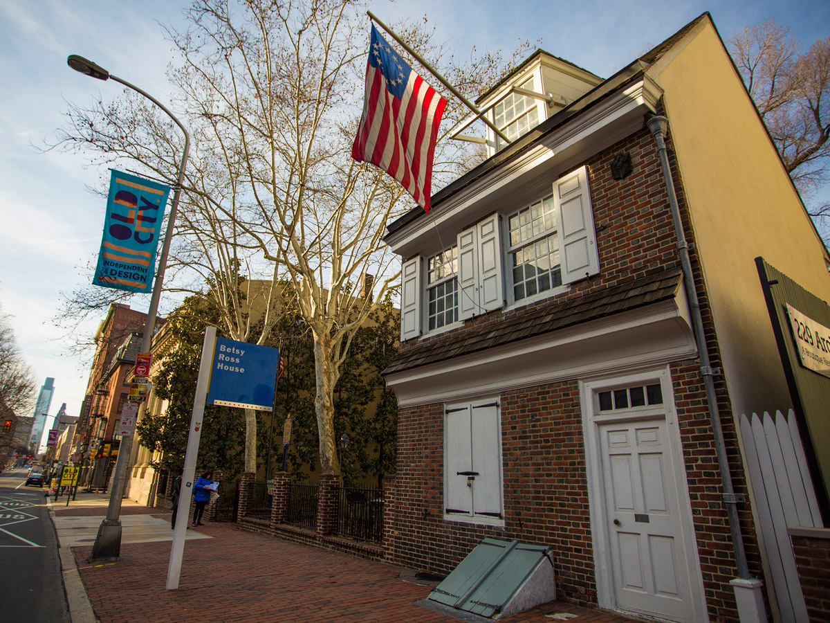 The brick exterior of the Betsy Ross House with a sign on the sidewalk outside.
