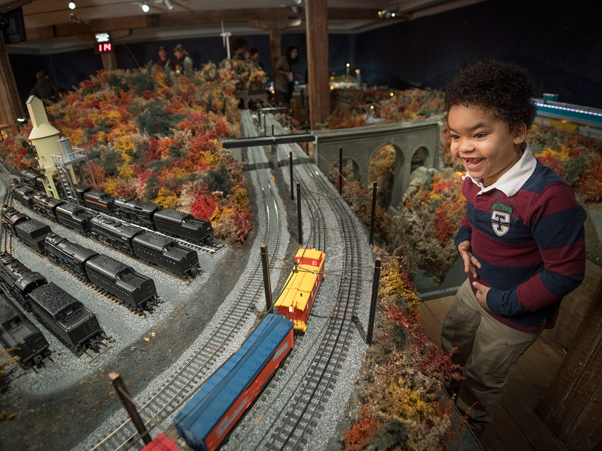 A young boy grins widely, showing his missing front teeth, as he watches the holiday train display ride by.