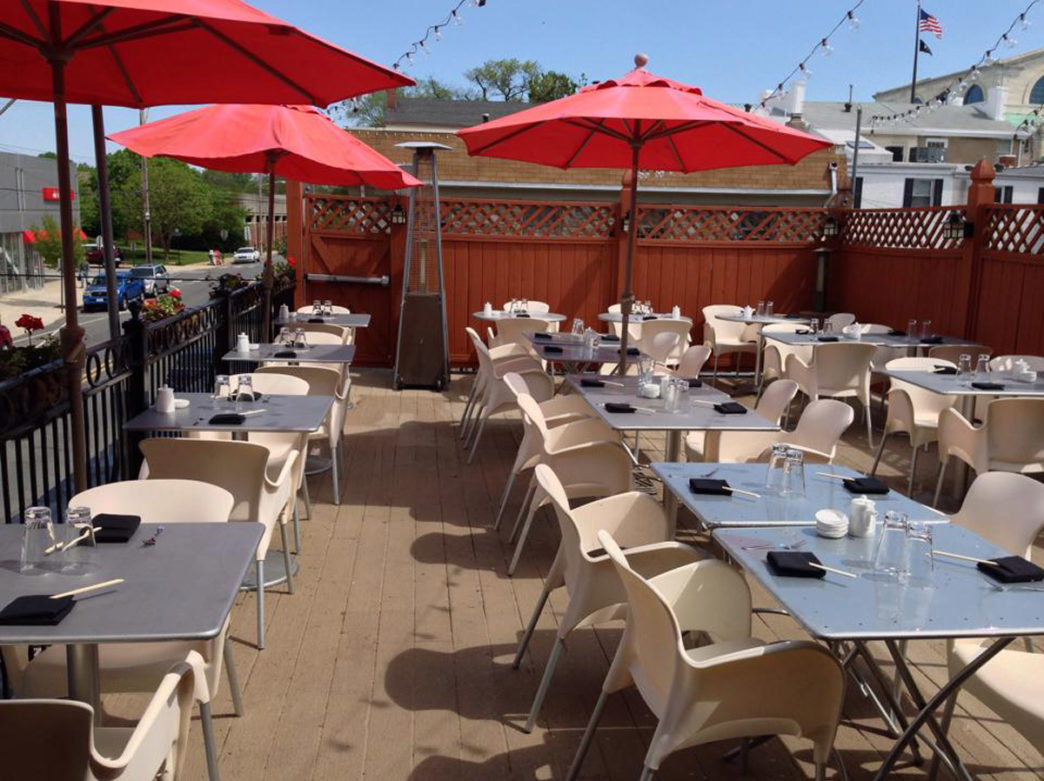 The roof deck at Azie in Media, Pennsylvania, featuring red umbrellas, metallic silver tables, and white chairs on a sunny day.