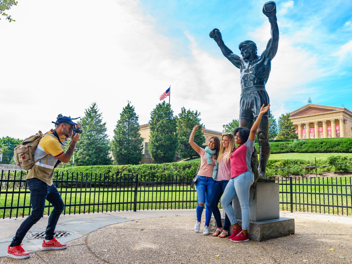 Three women pose in front of the Rocky Statue in Philadelphia while they have their picture taken