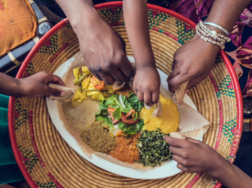 Five hands holding bread dipping into a dish at the center of a table