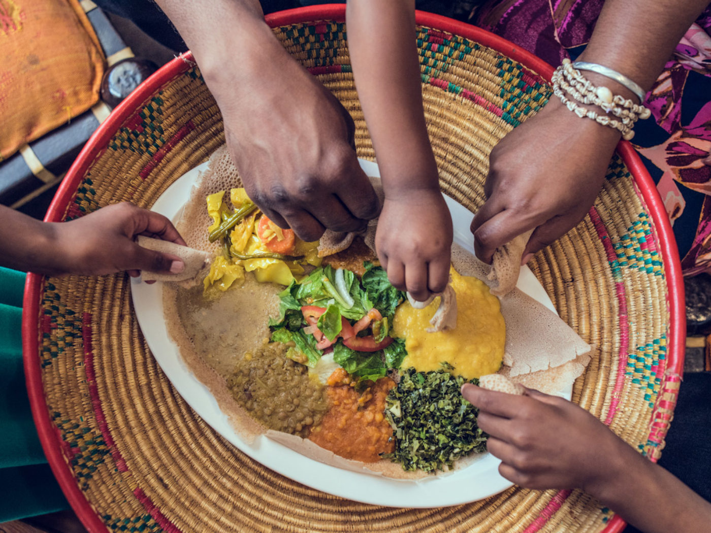 Five hands holding bread dipping into a dish at the center of a table