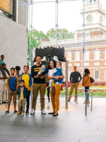 A man takes a photo of a family posing in front of the Liberty Bell in Philadelphia