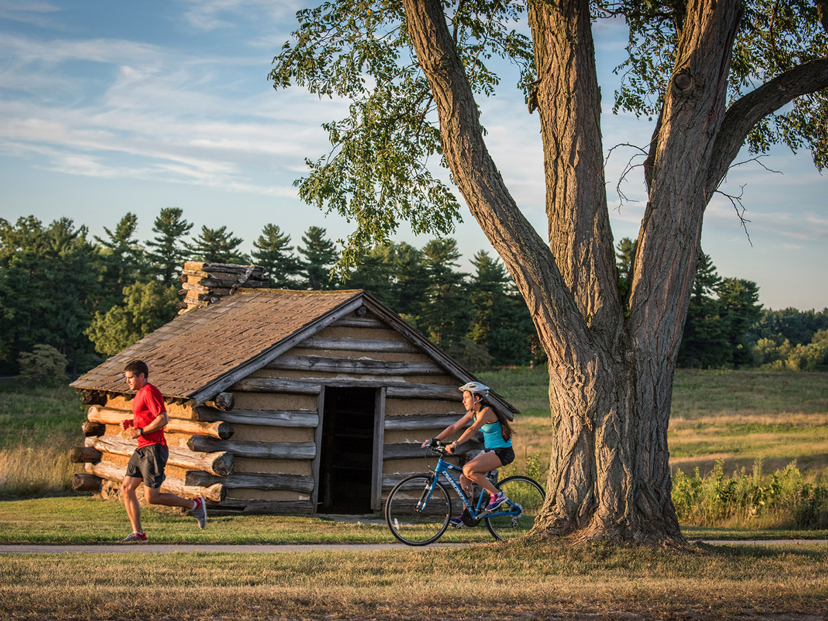 Un homme court et une femme fait du vélo sur les pistes de Valley Forge National Historical Park