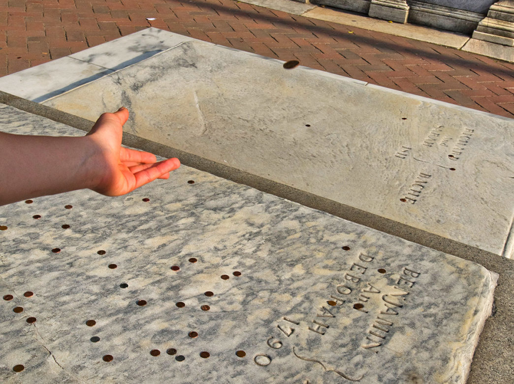 A ahdn throws a penny on Ben Franklin's grave at the Christ Church Burial Ground in Philadelphia
