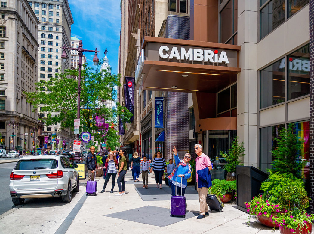 An older couple with suitcases standing outside the Cambria Hotel in downtown Philadelphia