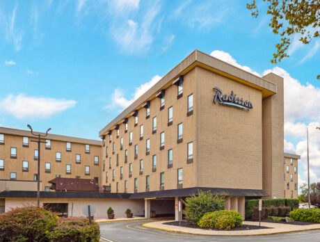 Exterior shot of the Radisson Hotel Philadelphia Northeast. A blue sky is in the background, with green bushes in the foreground