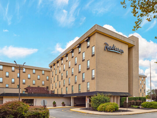 Toma exterior del Radisson Hotel Philadelphia Northeast. Se ve un cielo azul al fondo y arbustos verdes en primer plano.