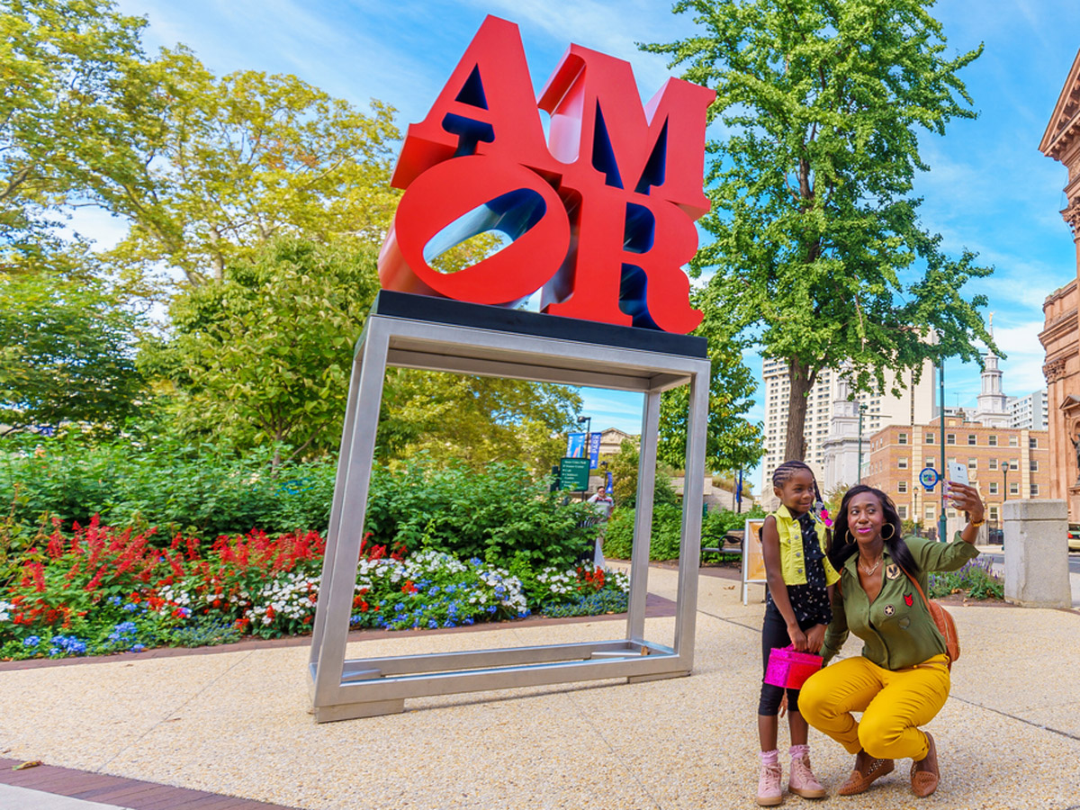 A mother and her young daughter take a selfie in front of the Amor statue in Center City Philadelphia