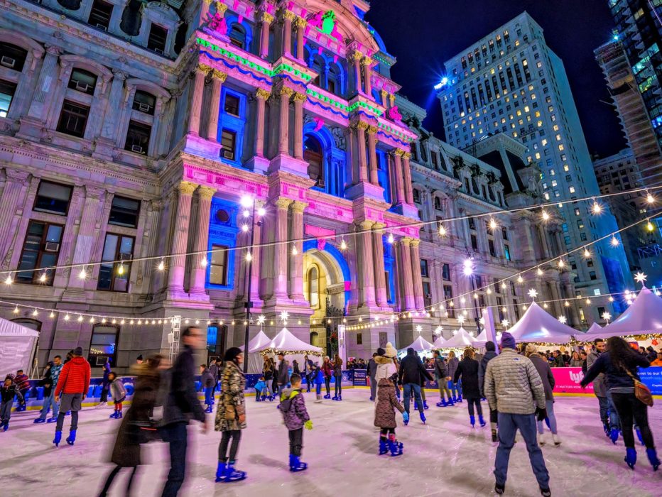 People ice skate below a light show on City Hall