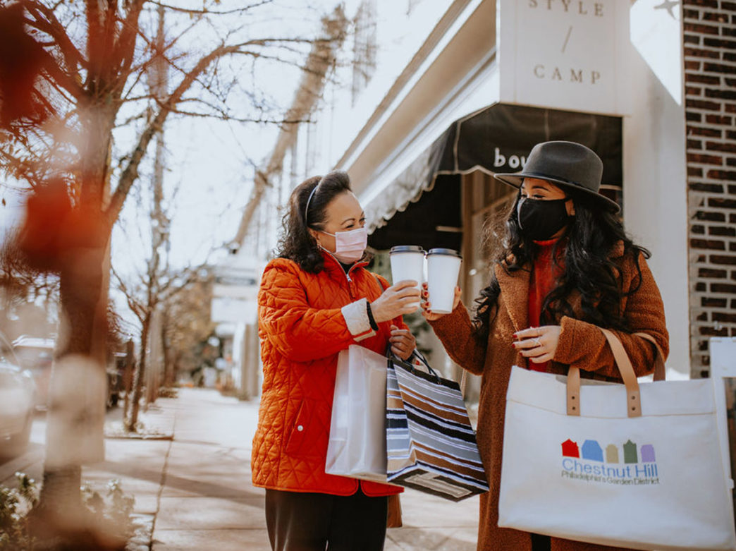 Two women wear Covid-19 masks as they carry coffee and shopping bags in Chestnut Hill, Philadelphia
