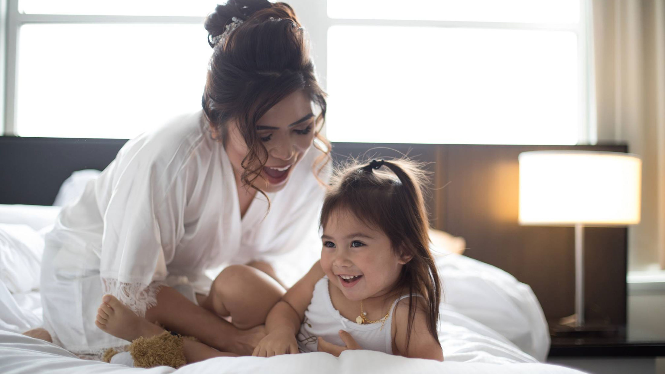 A mom and daughter play on a hotel bed at the Loews Philadelphia Hotel