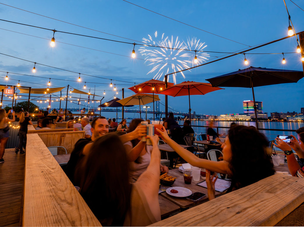 A group of people toasts while fireworks go off in the background at Liberty Point in Philadelphia