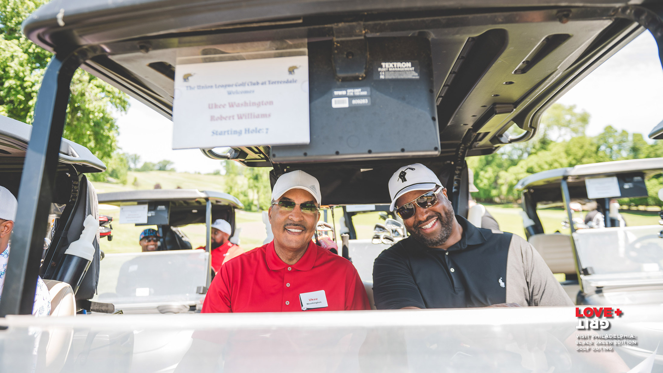 Two people sitting in a golf cart smile for the camera