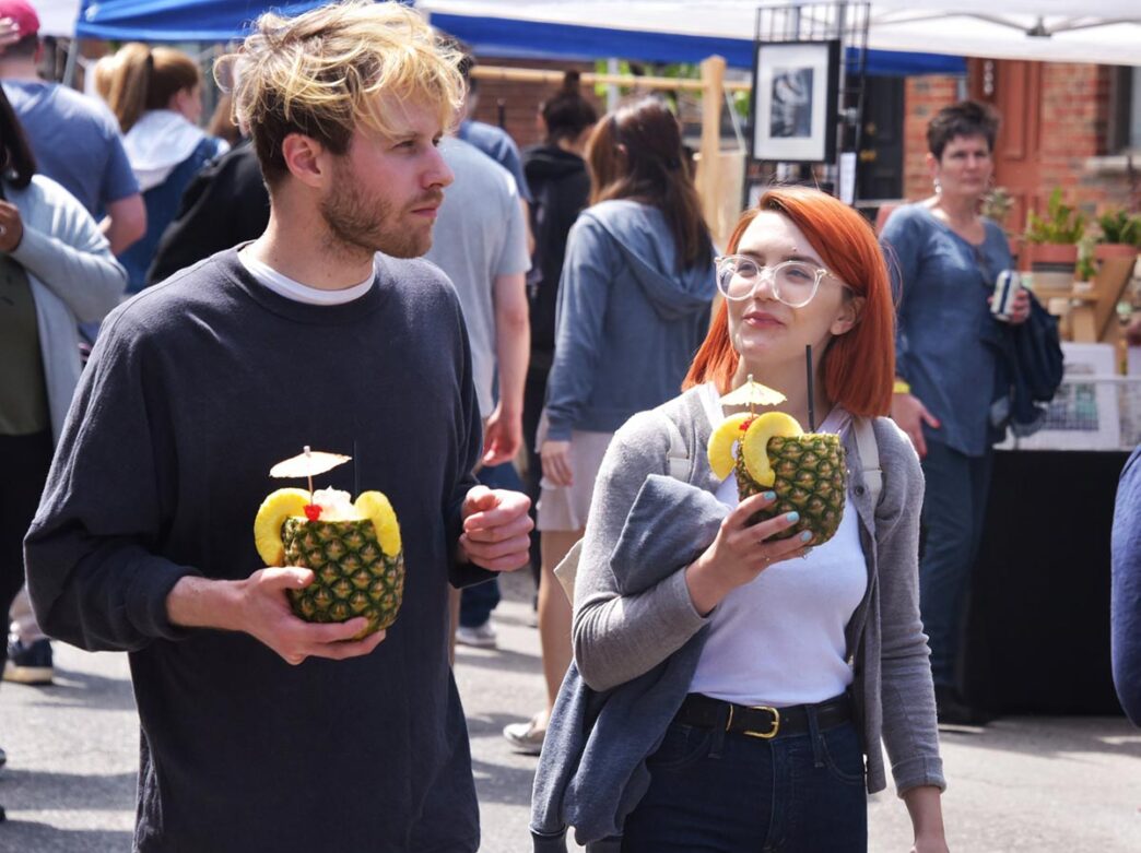 A man and woman carry pineapple cocktails at Flavors on the Avenue