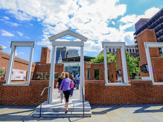 A person walks into the outline of The President's House under blue skies in Philadelphia