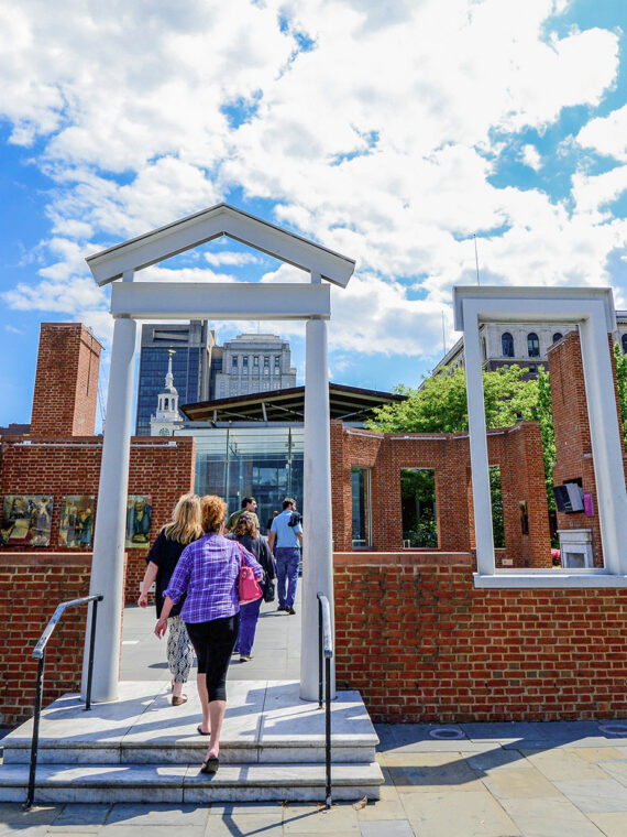 A person walks into the outline of The President's House under blue skies in Philadelphia