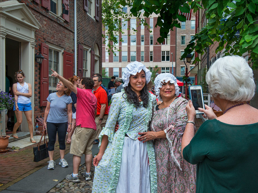 Two women dressed in colonial garb pose for a photo during Fete Day at Elfreth's Alley