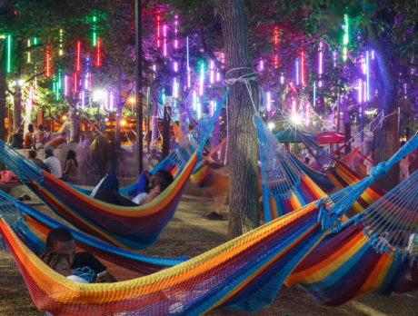 People lounge in colorful hammocks underneath brilliant lights at Spruce Street Harbor Park in Philadelphia