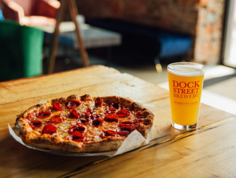 A pizza and a beer sit on a wooden table in the sunlight at Dock Street Brewery in Philadelphia's Point Breeze neighborhood