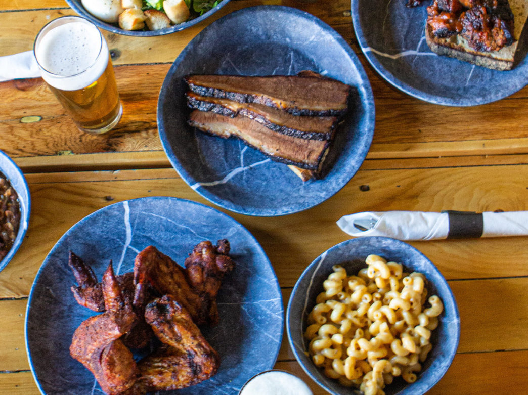 An overhead shot of food at beer on a wooden table at La Cabra Brewing