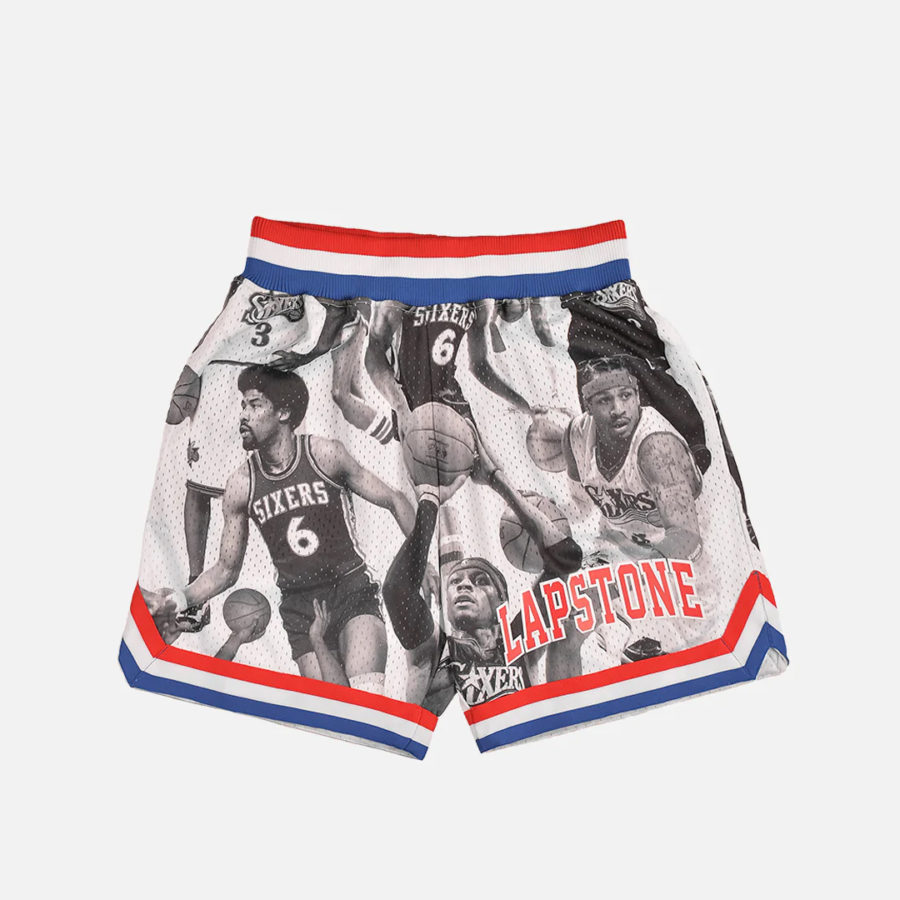 A pair of shorts against a gray background. The shorts feature photos of famous players for the Philadelphia 76ers, including Allen Iverson. The wasitband of the shorts is red, white and blue.