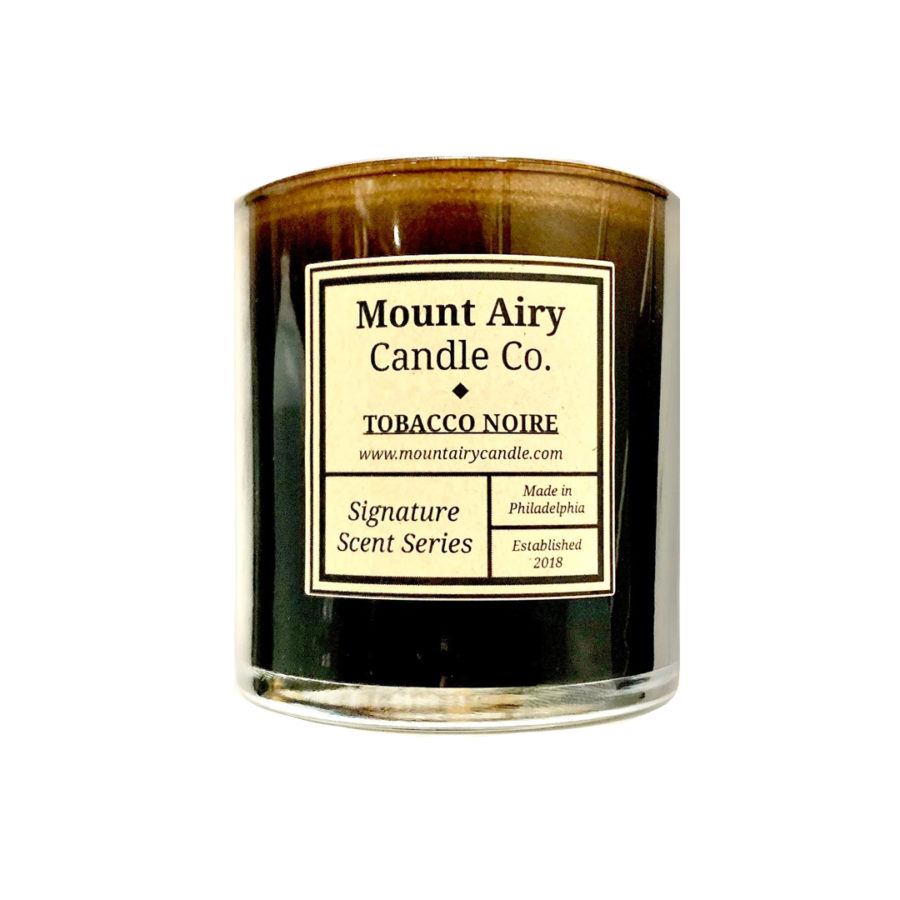 A dark candle against a white background. The candle has a tan sticker that says, in part, Mount Airy Candle Co. Tobacco Noire.