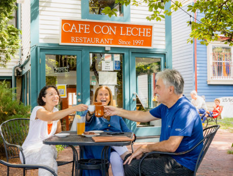 Three diners seated at an outdoor table toast with coffee mugs at Cafe Con Leche in Newtown