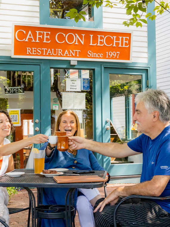 Three diners seated at an outdoor table toast with coffee mugs at Cafe Con Leche in Newtown