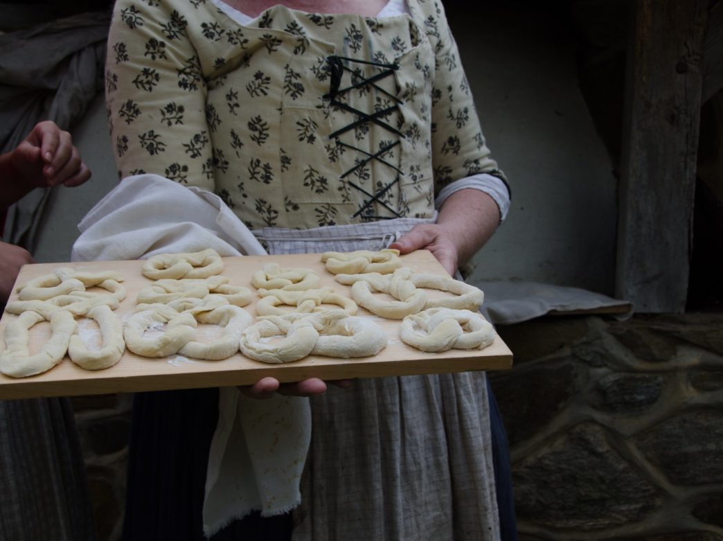 A historic re-enactor holds a tray of uncooked dough ready for baking