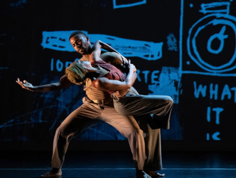 Two people dance in front of a backdrop with drawings on it
