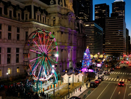 A Ferris wheel lights up in red next to shopping huts and the Holiday TRee at Dilworth Park in Philadelphia