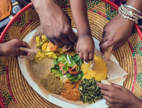 Five hands holding bread dipping into a dish at the center of a table