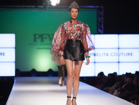 A woman in a colorful top and leather skirt walks down the runway during a fashion show