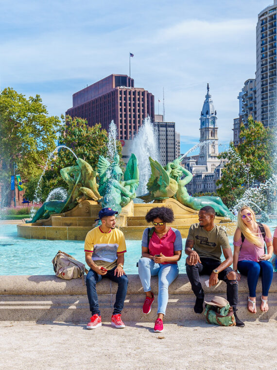 People sit on the edge of a fountain in Logan Square on a beautiful day in Philadelphia