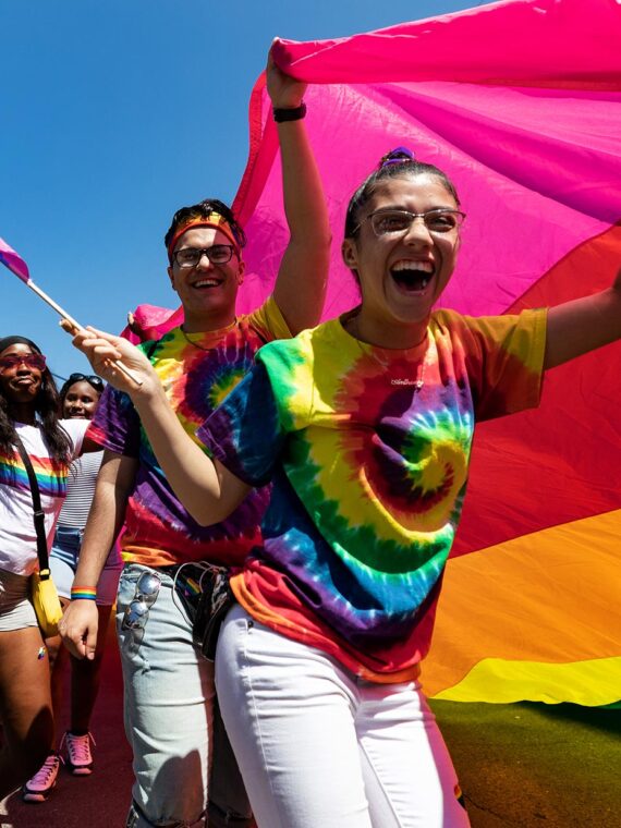 A group of people smiling and carrying a large rainbow Pride flag during the New Hope Celebrates PrideFest