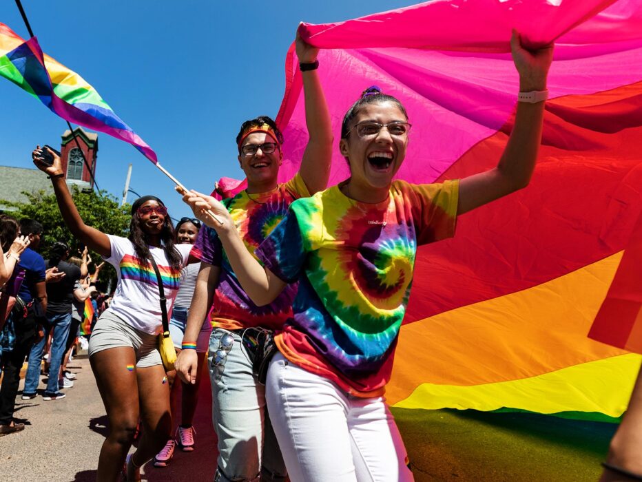 A group of people smiling and carrying a large rainbow Pride flag during the New Hope Celebrates PrideFest