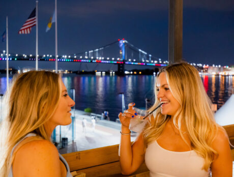 Two people smile and drink with the Benjamin Franklin Bridge in the background at Liberty Point in Philadelphia