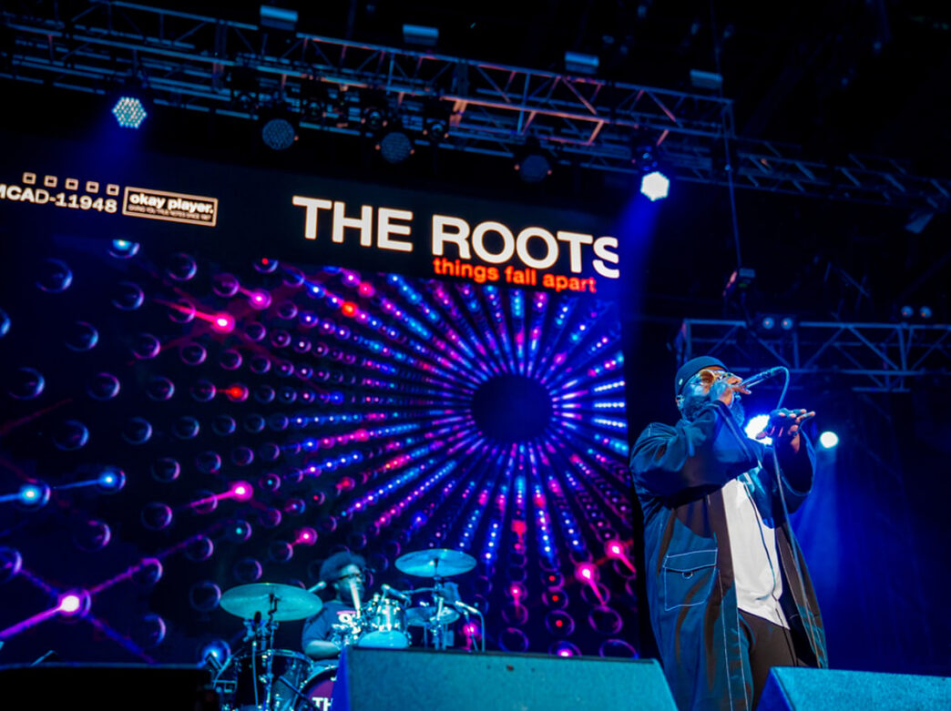 Black Thought of The Roots raps onstage at The Roots Picnic while Questlove plays the drums in the background.