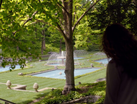 A person standing in the shadows looks out at the well-lit gardens in Longwood Gardens