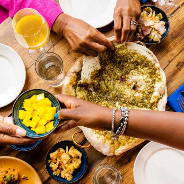 An overhead shot of people handing each other dishes at a restaurant table.