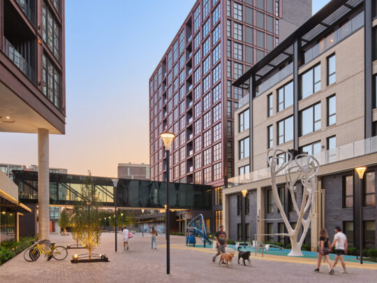 People walk through the courtyard between gleaming buildings at the Piazza in Philadelphia