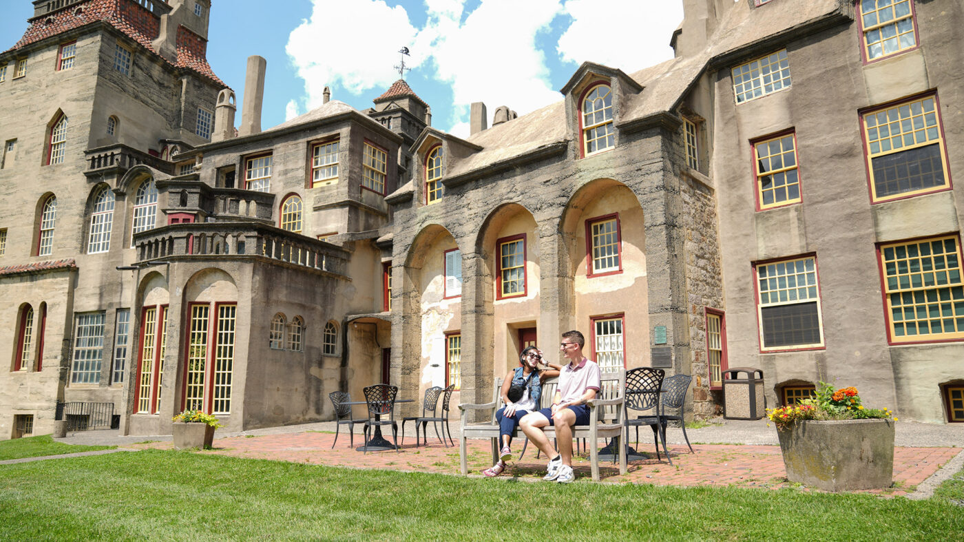 Two people sit on a bench on a clear blue day with the castle in the background.