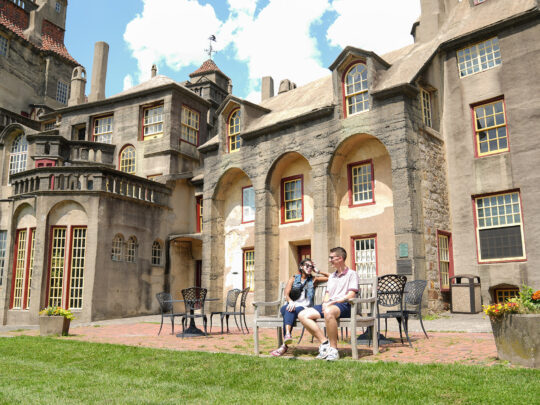 Two people sit on a bench on a clear blue day with the castle in the background.