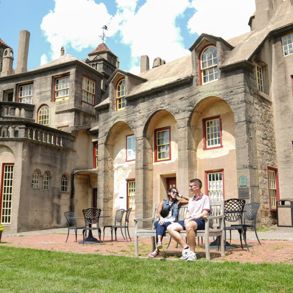 Two people sit on a bench on a clear blue day with the castle in the background.