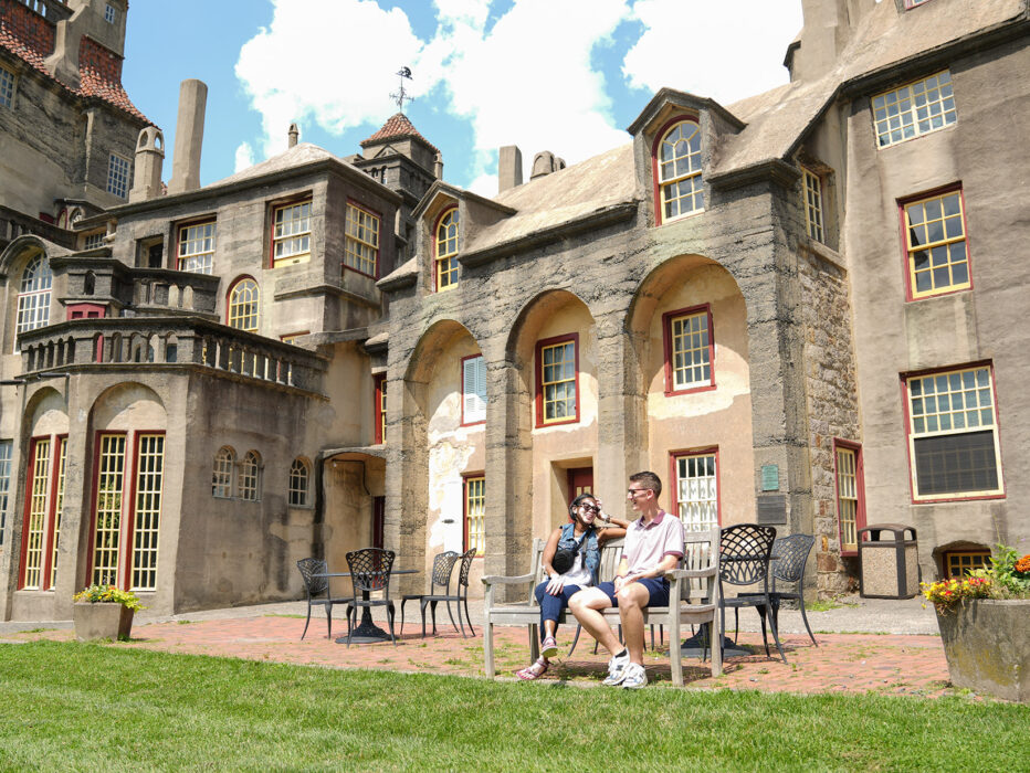 Two people sit on a bench on a clear blue day with the castle in the background.