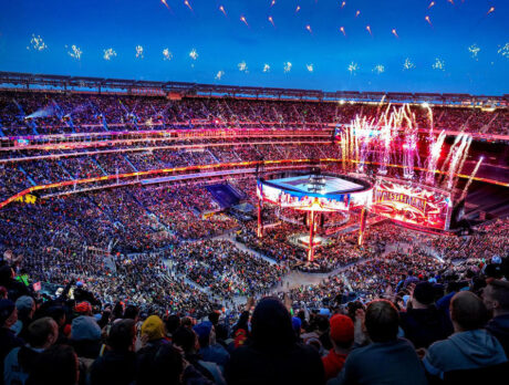 Fireworks explode in the sky above a large, packed stadium during WrestleMania.